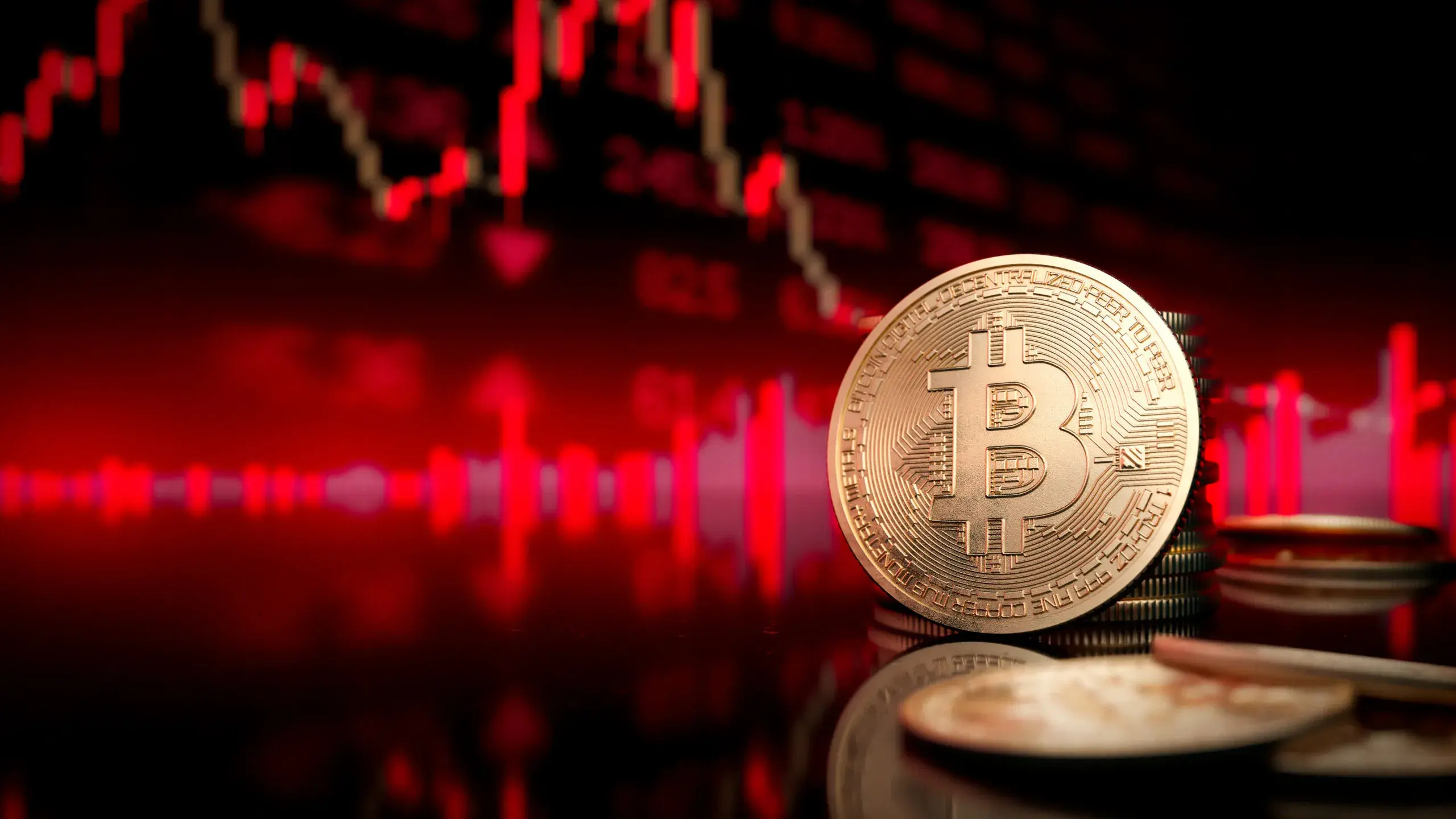 A gold Bitcoin coin standing in front of a blurred red market chart